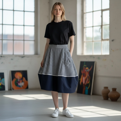 Woman wearing a black top and checkered skirt in a room with large windows and art on the walls.